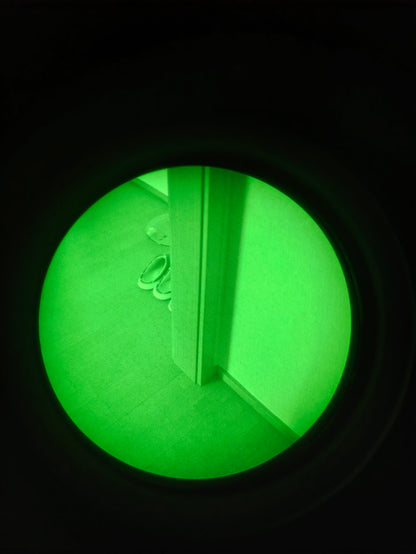New through-tube indoor scene photographed through a Kaelor Works BNVD-1431 ATOM green-phosphor binocular. Camera colour and brightness may differ from direct viewing.