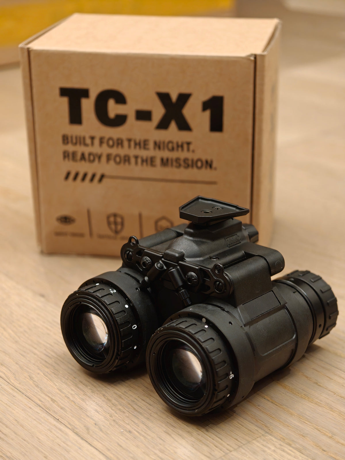 TC-X1 night vision binocular photographed in front of TC-X1 packaging